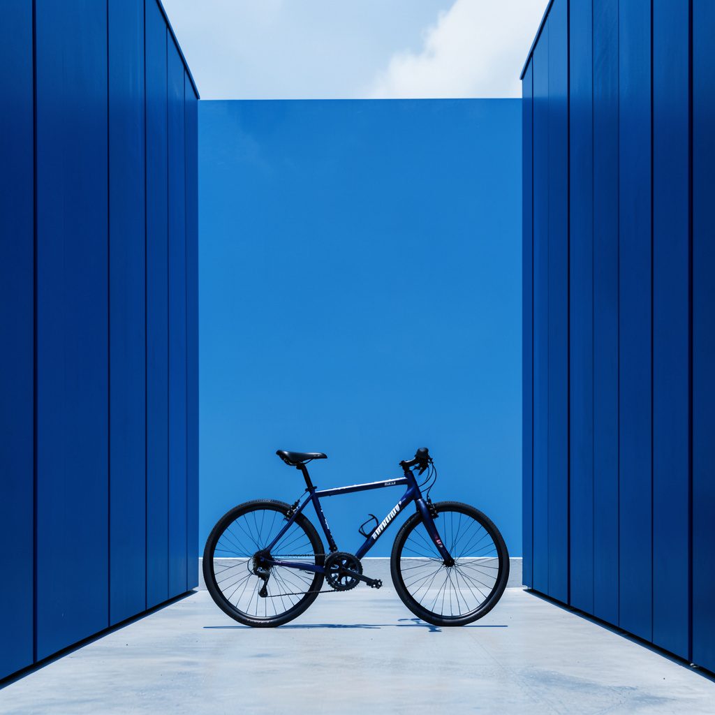 A sweeping Idaho landscape with rolling green hills under a wide blue sky, a winding two-lane road cutting through the countryside toward distant mountains.